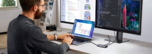 Développeur travaillant avec un écran externe large et un hub USB-C, deux des meilleurs accessoires tech pour un espace de travail productif