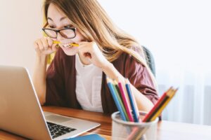 femme mordant un crayon alors qu'elle est assise sur une chaise devant un ordinateur pendant la journée